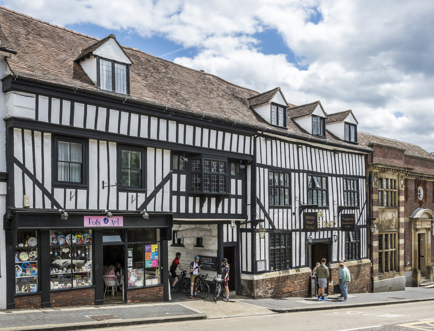 The historic White Hart Hotel in St Albans, its black-and-white timbered fa&ccedil;ade standing out along a city centre street beneath a bright sky.
